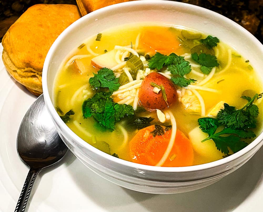 Mamá's Lime and Cilantro Chicken Noodle Soup in a bowl with oven-baked biscuits. 