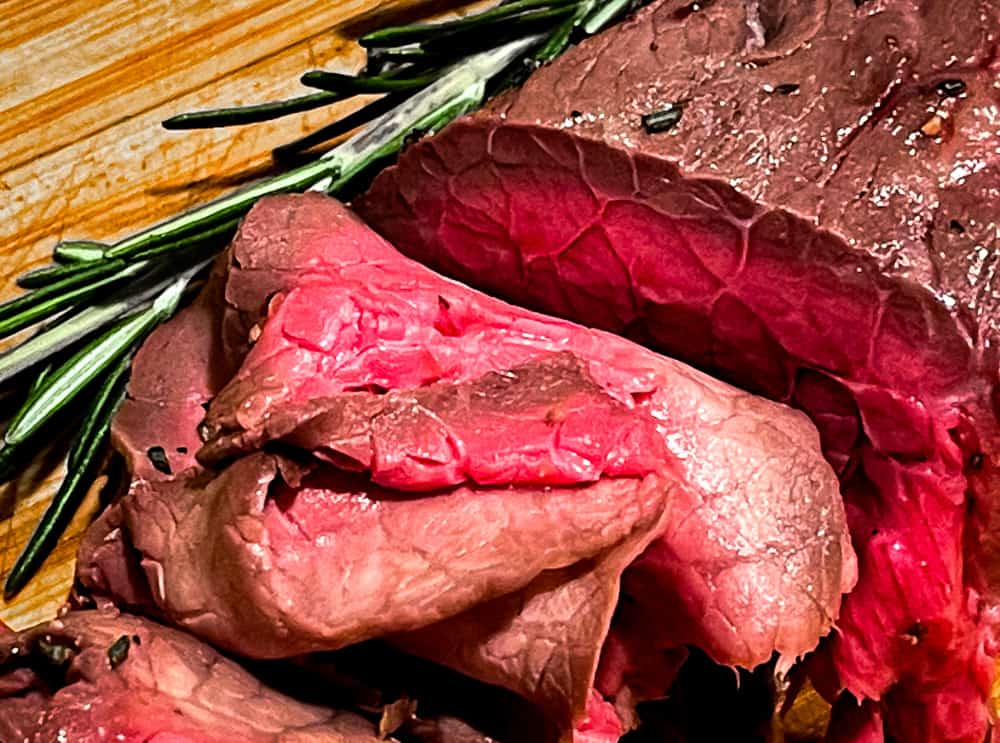 Closeup of thinly sliced roast beef with rosemary. 