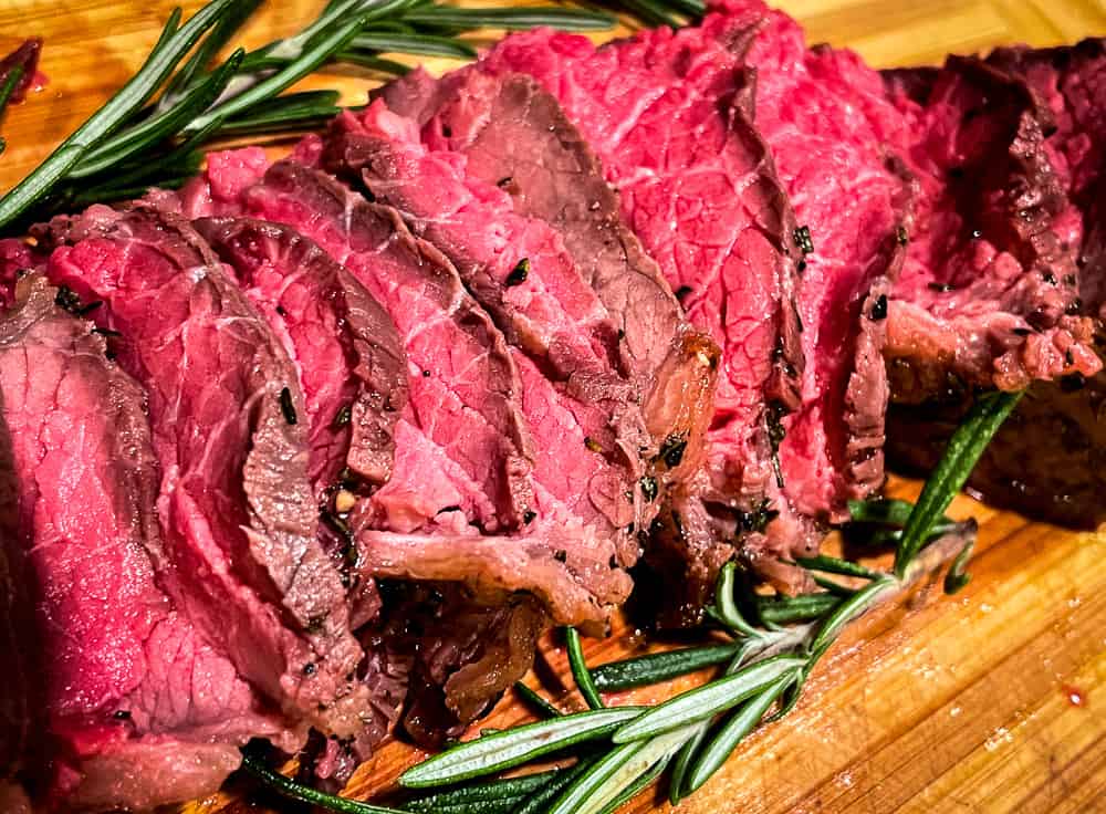 Thinly sliced roast beef with rosemary on a cutting board