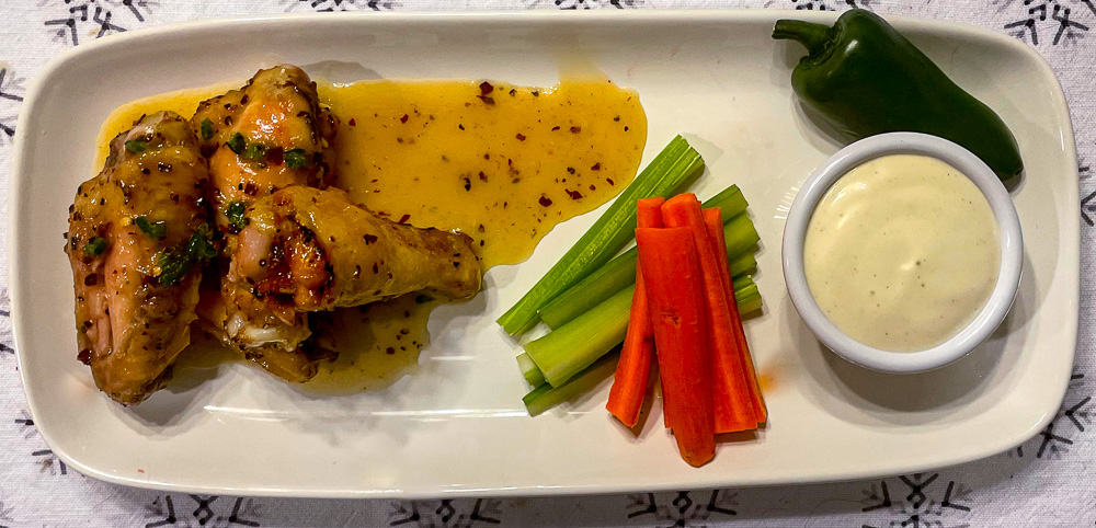 Hot pepper honey wings on a plate with carrots, celery, jalapeño pepper, and ranch dressing.
